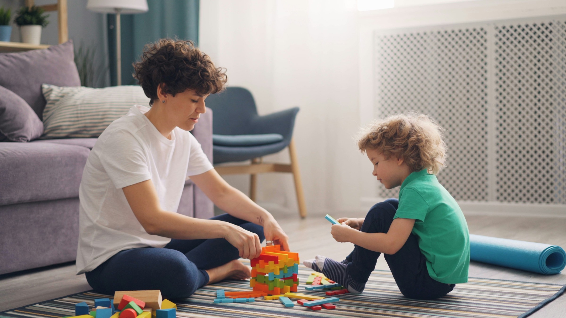 An adult and a young child building towers of blocks together on a living room floor